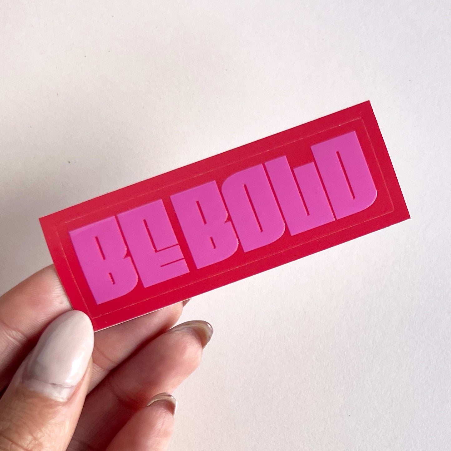 red and pink be bold sticker, held in hand